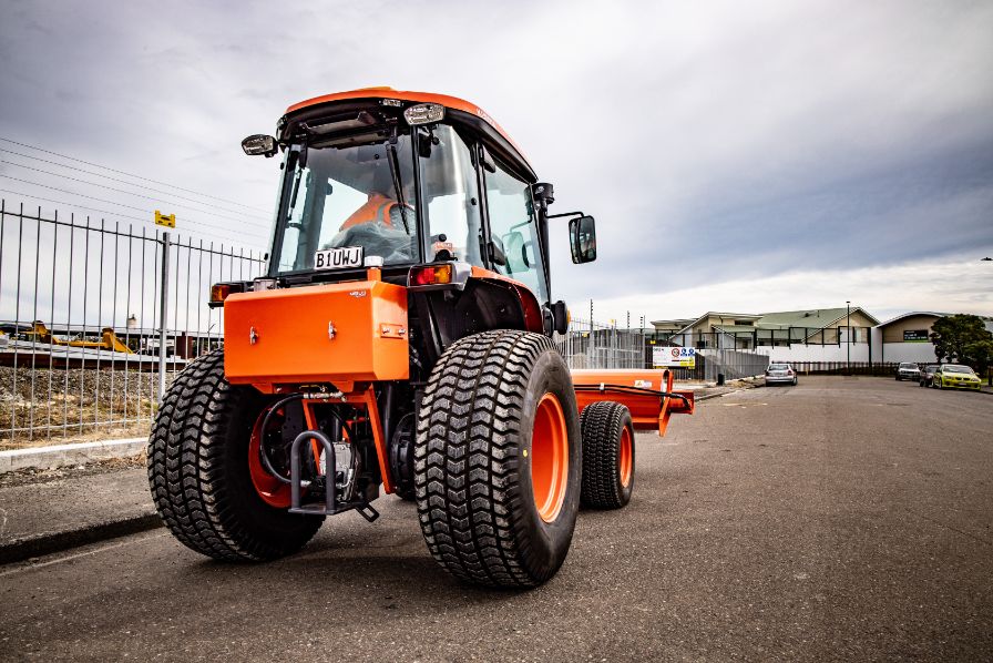 Rear view of Orange Kubota Tractor sweeper, sweeping driving along the road